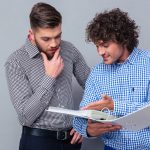 Two men looking at notebook and discussing it