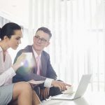 Businessman & businesswoman discussing over laptop with coffee