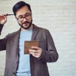 A man holding a pad scratching his head with a pen