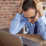man leaning over a desk with his hands head